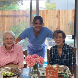 A warm gathering over lunch with seniors and their caregiver, enjoying meals and flowers.