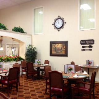 A cozy dining area with neatly arranged tables and chairs, a decorative clock on the wall, and indoor plants enhancing the ambiance.