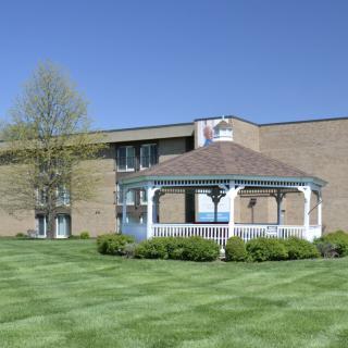 A white gazebo on a well-maintained lawn in front of a brick building under a clear blue sky.
