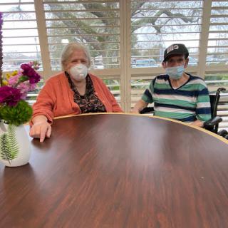 Two individuals enjoying a moment together indoors, amidst a cozy setting with flowers.