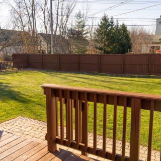 A sunny backyard with a wooden deck and a well-maintained lawn, enclosed by a fence.