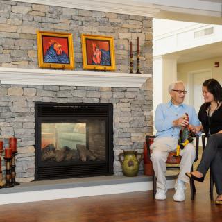 Two people seated near a stone fireplace in a cozy living room setting.