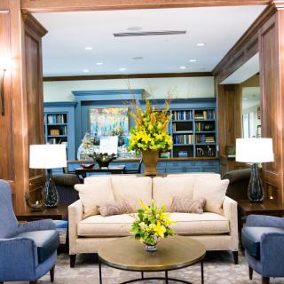A cozy lobby area with a sofa, armchairs, and bookshelves, elegantly decorated with flowers and soft lighting.