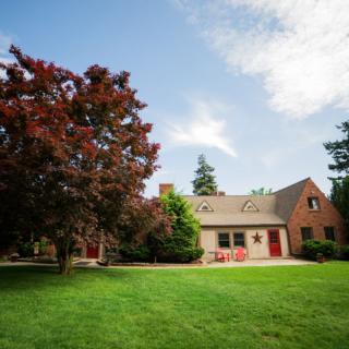A picturesque house with a large yard, surrounded by trees and under a clear sky.