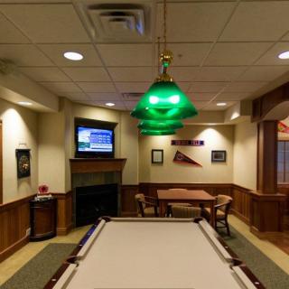A cozy game room featuring a billiards table, a television mounted on the wall, and warm lighting with a green pool table lamp.