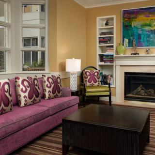 A cozy living room with a vibrant sofa and decorative pillows, featuring a fireplace and colorful artwork.
