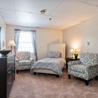 A cozy bedroom with a bed, two patterned chairs, and soft lighting.
