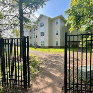 View of an apartment building through an open gate, surrounded by greenery.