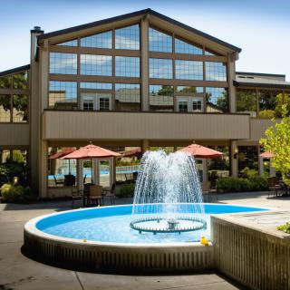 A modern building with large glass windows and an outdoor patio featuring a circular fountain.