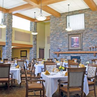 A well-decorated dining area with neatly arranged tables and chairs, featuring a stone fireplace and warm lighting.
