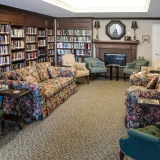 A cozy library reading room with sofas and bookshelves surrounding a fireplace.