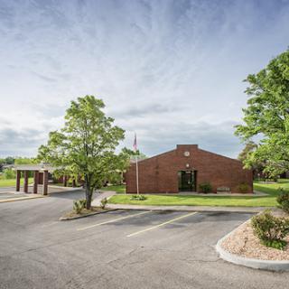 A brick building surrounded by trees and a clear parking area under a cloudy sky.