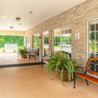 A covered porch area with benches, plants, and windows along a brick wall.