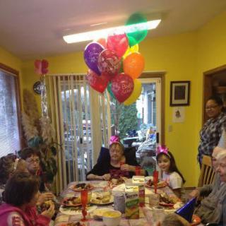 A cheerful birthday celebration with children gathered around a table, colorful balloons overhead, and family members enjoying the special occasion.