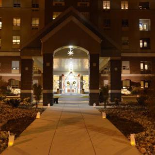 A beautifully illuminated entrance of a building at night, showcasing architectural details and a welcoming pathway.