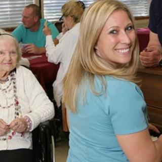 A cheerful interaction between a caregiver and an elderly woman in a care facility.