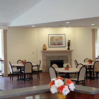 A cozy dining area with round tables, chairs, and a fireplace decorated with vases and paintings.