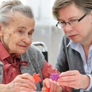 An elderly woman receiving assistance with a puzzle from a caregiver.