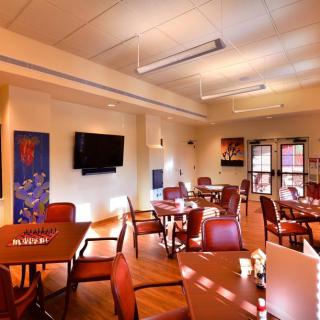 A well-lit dining room with multiple tables and chairs, featuring a wall-mounted television and decorative artwork.