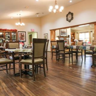 A spacious dining room with wooden flooring, neatly arranged tables and chairs, and elegant lighting.
