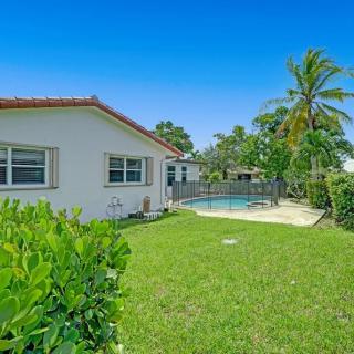 A beautiful house with a lush green lawn, a swimming pool, and palm trees under a clear blue sky.
