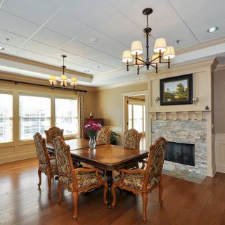 A beautifully designed dining room featuring a wooden table and ornate chairs, with a fireplace adorned with artwork and elegant chandeliers lighting the space.