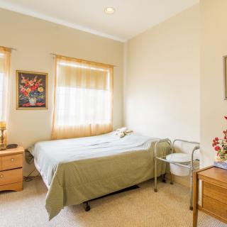 A cozy bedroom with a single bed, decorated with artwork and featuring a nightstand and chair by the window.