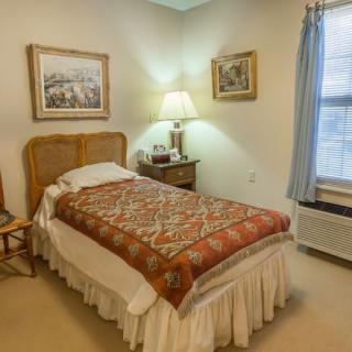 A cozy bedroom with a single bed, lamp, and window next to a side table adorned with framed artwork.