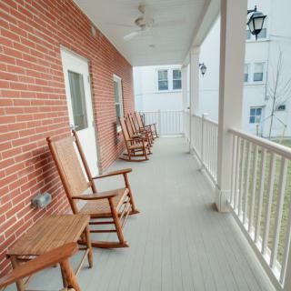 A spacious porch with wooden rocking chairs and a white railing, set against a brick wall.