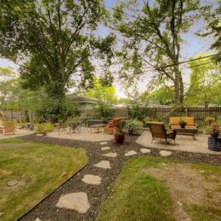 A serene backyard garden with a patio area and outdoor seating, surrounded by lush greenery and mature trees.