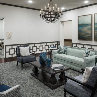 A stylishly furnished living room featuring a chandelier, sofa, armchairs, and a coffee table with decorative items.