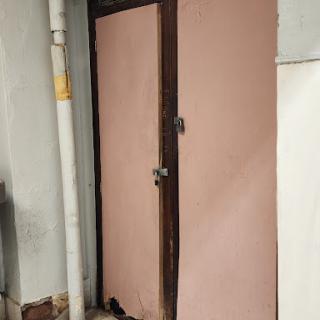A wooden door with a pink surface, framed within the wall of a building.