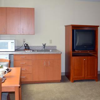 A small kitchen area with wooden cabinets, a microwave, and a TV cabinet.