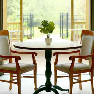 A cozy dining area with a round table, two wooden chairs, and a small potted plant, illuminated by natural light.