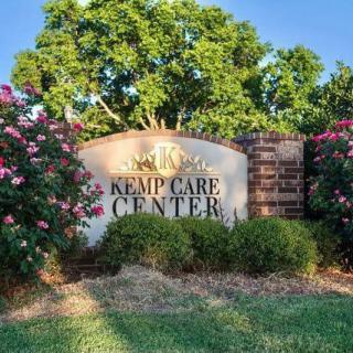 A sign for Kemp Care Center surrounded by vibrant flowers and lush greenery.