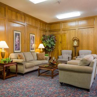 A cozy living room with traditional decor, featuring comfortable sofas and armchairs, wooden paneling, and decorative indoor plants.