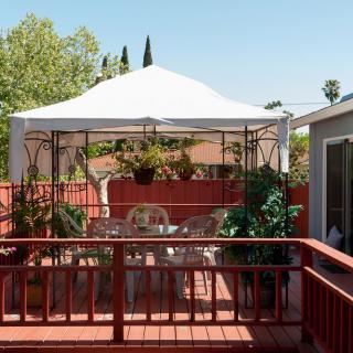 A cozy patio with a gazebo, surrounded by plants and outdoor furniture on a sunny day.