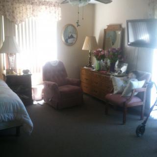 A cozy bedroom interior featuring a bed, chairs, dresser with mirror, and lamps.