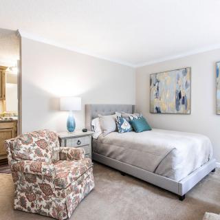 A cozy bedroom featuring a neatly made bed, floral armchair, and decorative artwork.