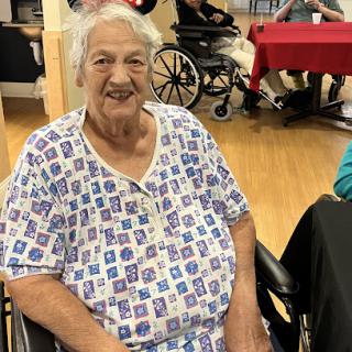 A cheerful elderly woman in a wheelchair, enjoying her time at a nursing home.