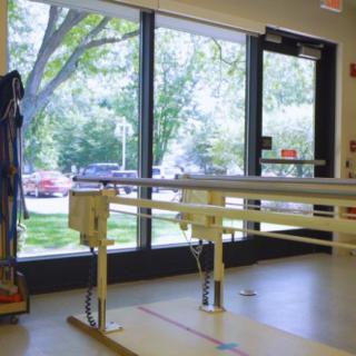 A physical therapy room equipped with parallel bars overlooking a window with a view of trees outside.