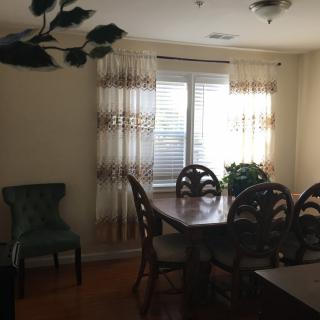 A cozy dining room with a wooden table, matching chairs, and a window with patterned curtains.