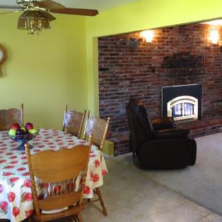 A cozy dining and living area with a brick fireplace and yellow walls.
