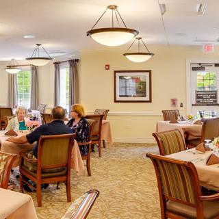 A cozy dining room with several tables and chairs, where people are enjoying a meal together.