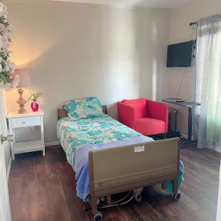 A cozy bedroom featuring a hospital bed, a red chair, and a small bedside table with a lamp.