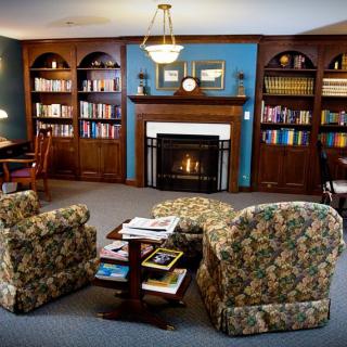 A cozy living room featuring a fireplace surrounded by filled bookshelves and two floral-patterned armchairs.