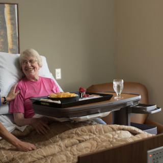 An elderly patient enjoying a meal with a caregiver in a hospital room.