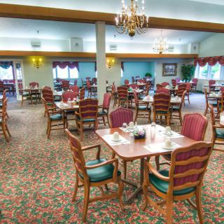An elegantly decorated dining room with multiple tables and chairs, featuring chandeliers and warm lighting.