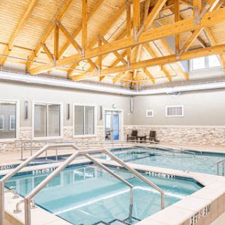 An inviting indoor swimming pool area featuring a spacious design with wooden beams and multiple pools for relaxation.