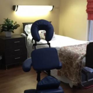 A cozy massage therapy room with a massage chair and bed.